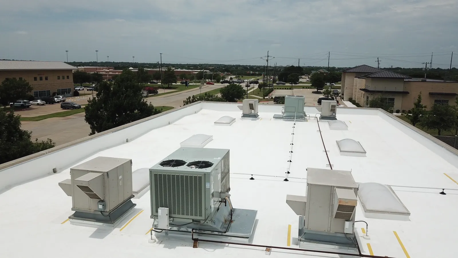 Drone view of a completed white TPO commercial re-roof with rooftop HVAC units, skylights and walkway pads in North Texas