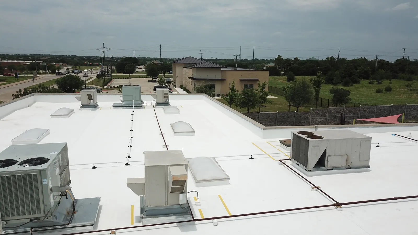 Aerial view of a finished white TPO roof with skylights, condensate lines on supports and yellow-marked walkway pads